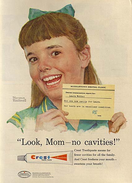 Big open smile on a girl with a green dress and green bow in her hair, holds up a note from the dentist, with Norman Rockwell's signature to the left and advertising copy below: Look Mom, no cavities. Crest Toothpaste means far fewer cavities for all the family. And Crest freshens your mouth - sweetens your breath!