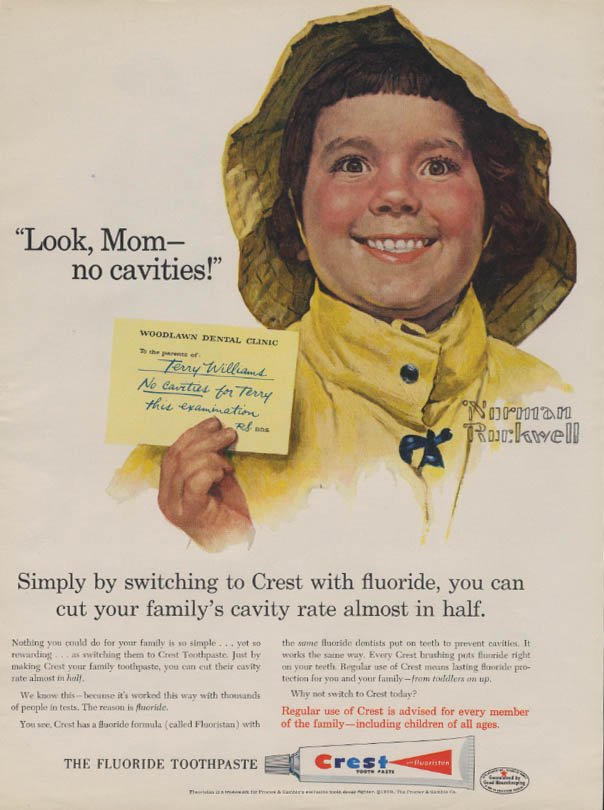 Mid-century magazine ad for Crest's stannous fluoride in toothpaste shows Norman Rockwell's drawing of little kid Terry Williams in a yellow rain hat and jacket, saying the slogan 'Look Mom no cavities,' and holding up a note from Woodlawn Dental Clinic saying 'To the proud parents of Terry Williams No cavities for Terry this examination.' Readable ad copy below: Simply by switching to Crest with fluoride, you can cut your family's cavity rate almost in half. Regular use of Crest is advised for every member of the family - including children of all ages. The fluoride toothpaste, plus a drawing of a tuble of Crest toothpaste.