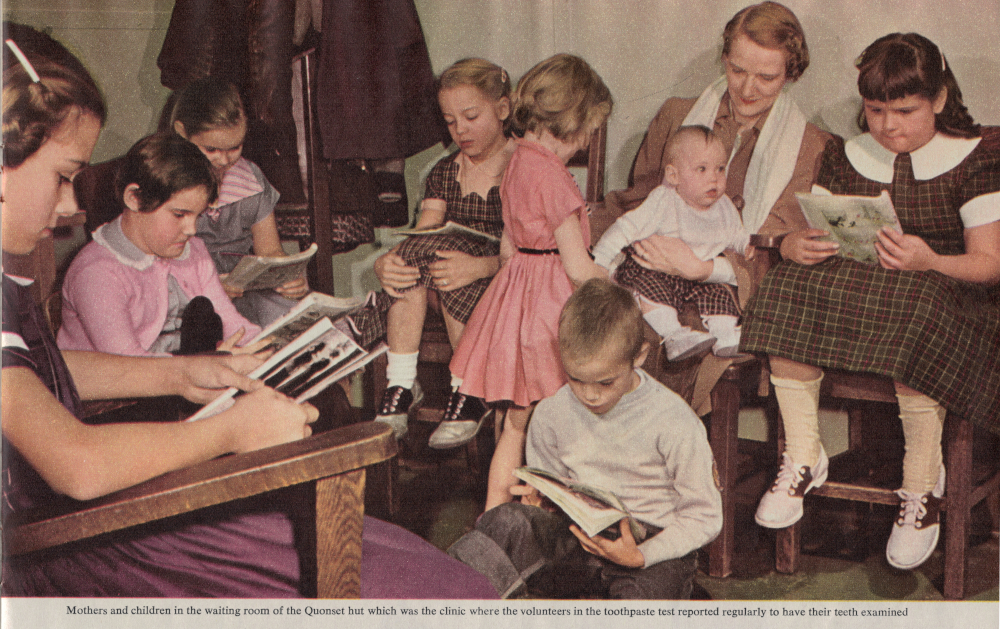 Color photograph from a 1950s magazine shows kids and parents waiting in a clinic. Five girls in clothes such as pink sweaters, Oxford shoes and checkered dresses sit in wooden chairs and read comic books and magazines. One boy on the floor reads a magazine. One girl in pink plays with a baby sitting on a mother's lap.